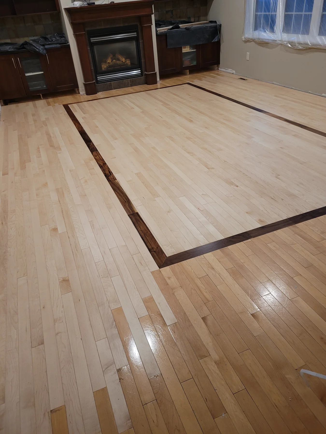 Living room hardwood floor with a custom walnut border inset framing new maple flooring near the fireplace